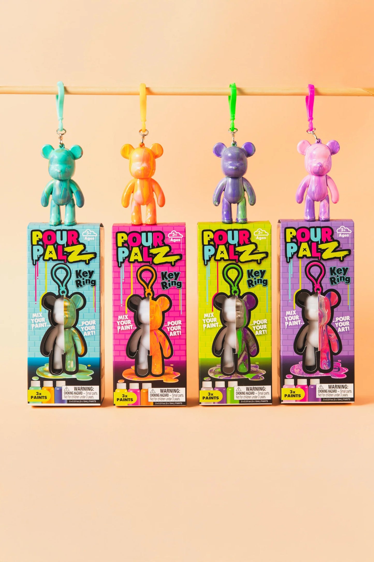 Pour Palz Mini Keyring Bear DIY Art Kits showing all 4 colour wave variants: teal, orange, purple and pink bears hanging above their boxes