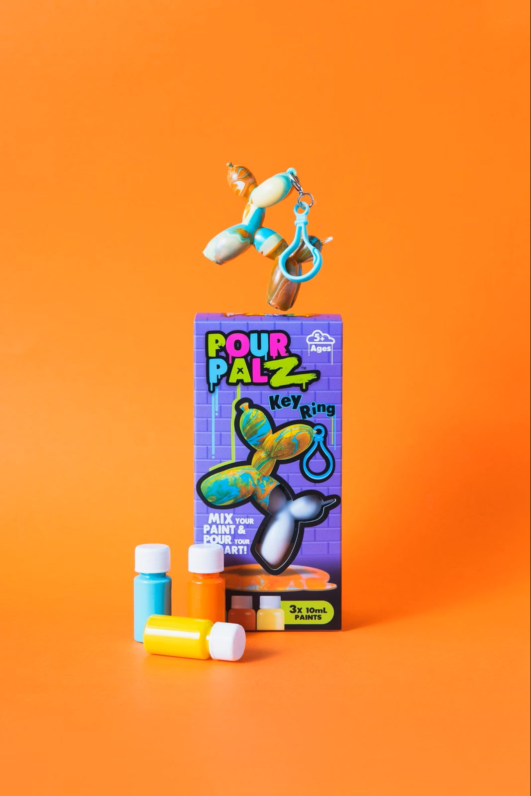 Pour Palz Mini Keyring Balloon Dog DIY Art Kit box with 3 paint bottles and a completed marbled teal and orange balloon dog keyring floating above on orange background